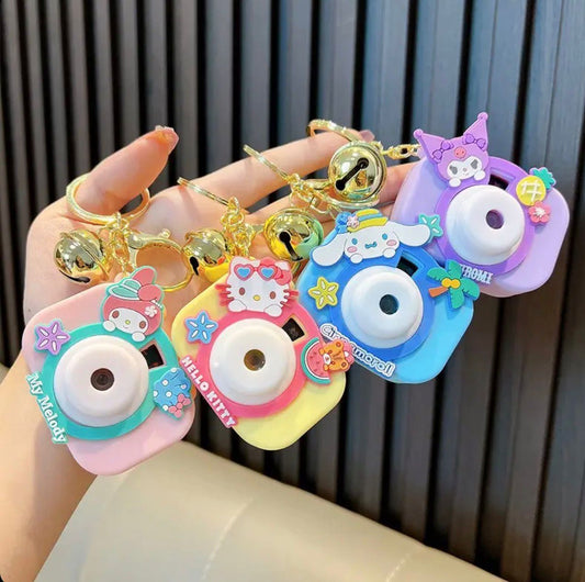 Hand holding pastel camera keychains with cartoon character toppers