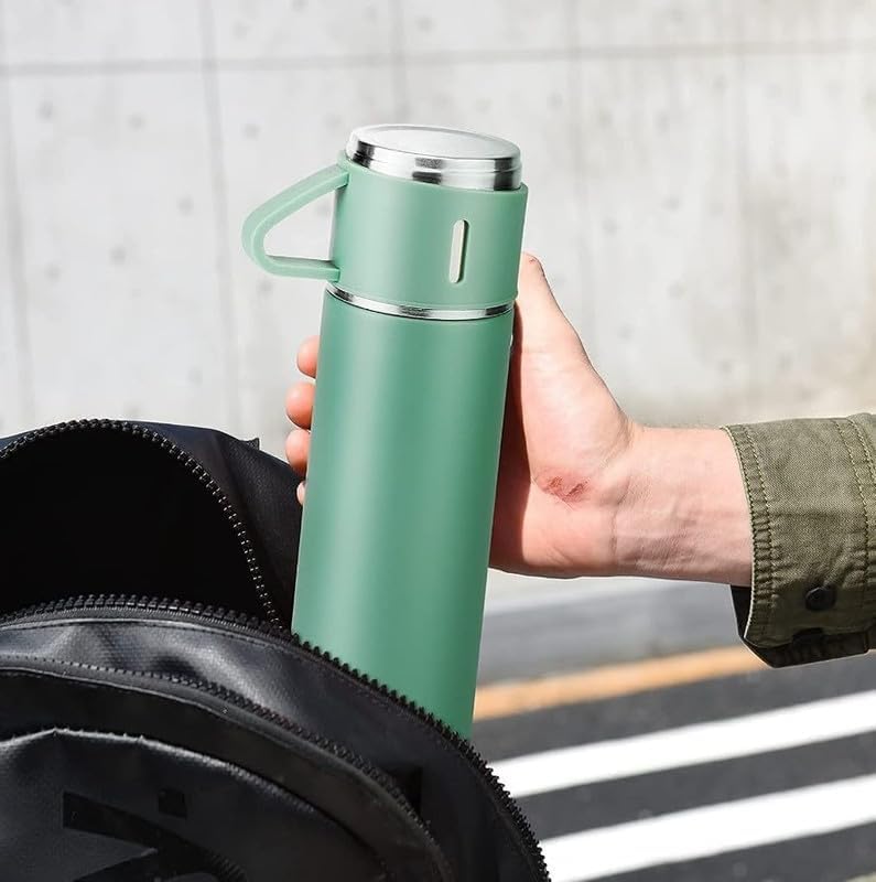 Hand holding a green 500ml vacuum flask beside a backpack