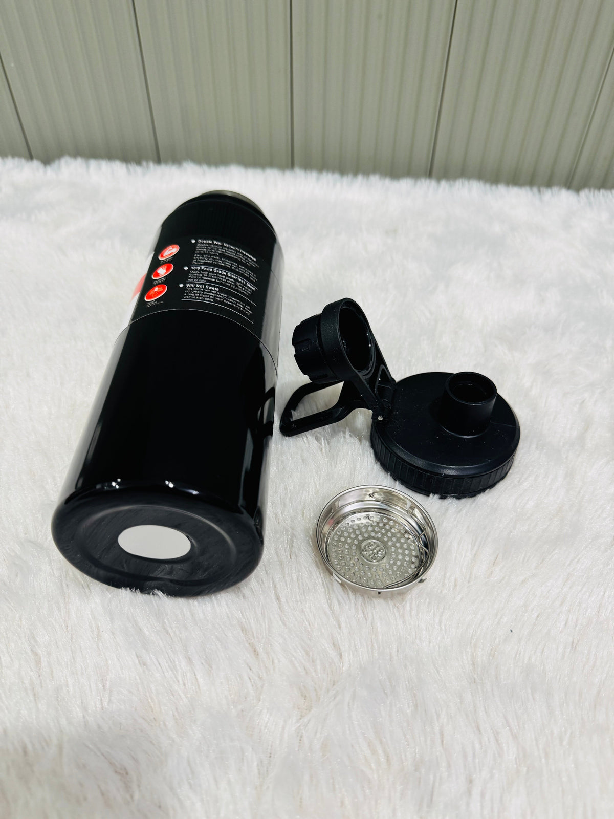 Black 800ml bottle lying down beside its lid and steel strainer