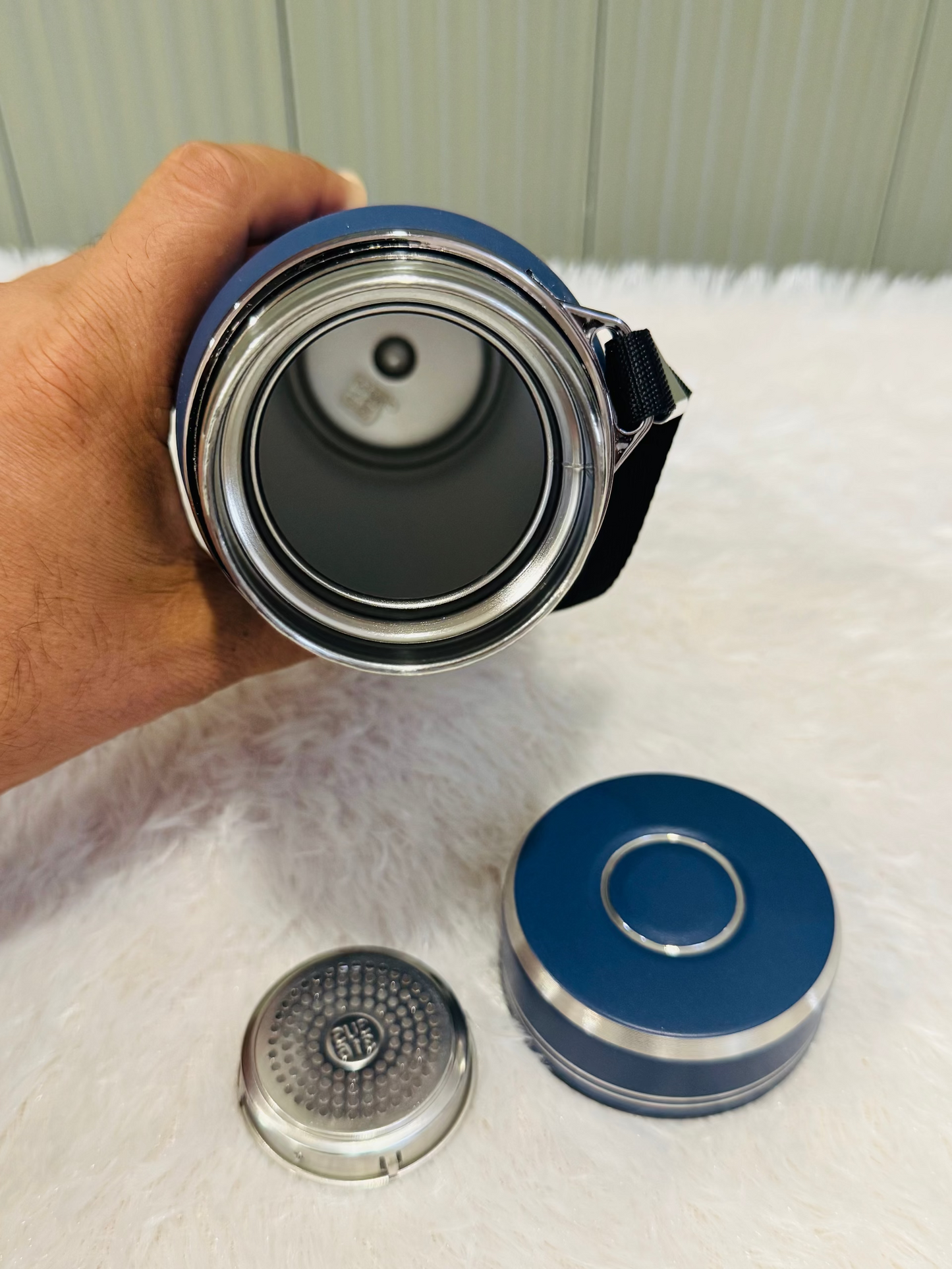 Hand holding an open navy 800ml bottle beside its lid and strainer