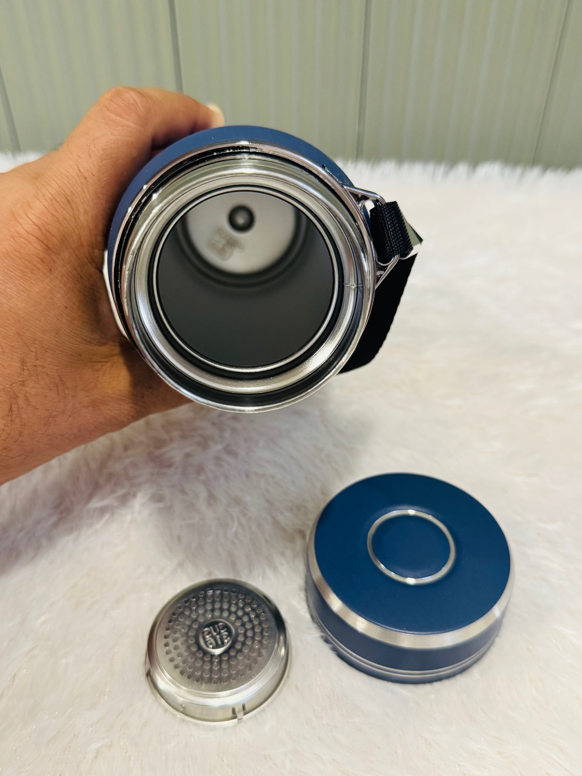 Hand holding an open navy 800ml bottle beside its lid and strainer