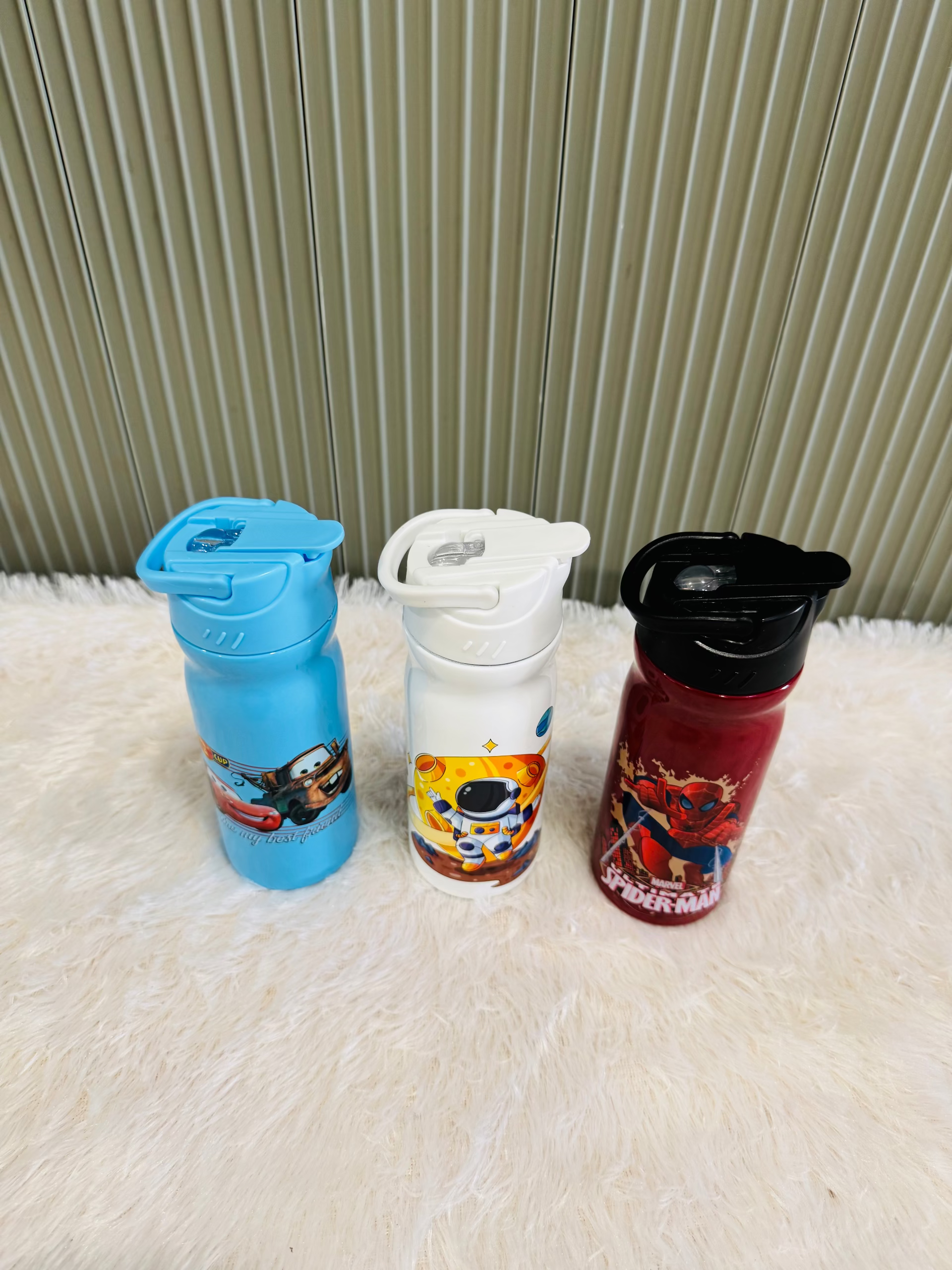 Three 400ml cartoon print kids bottles with flip lids on a rug
