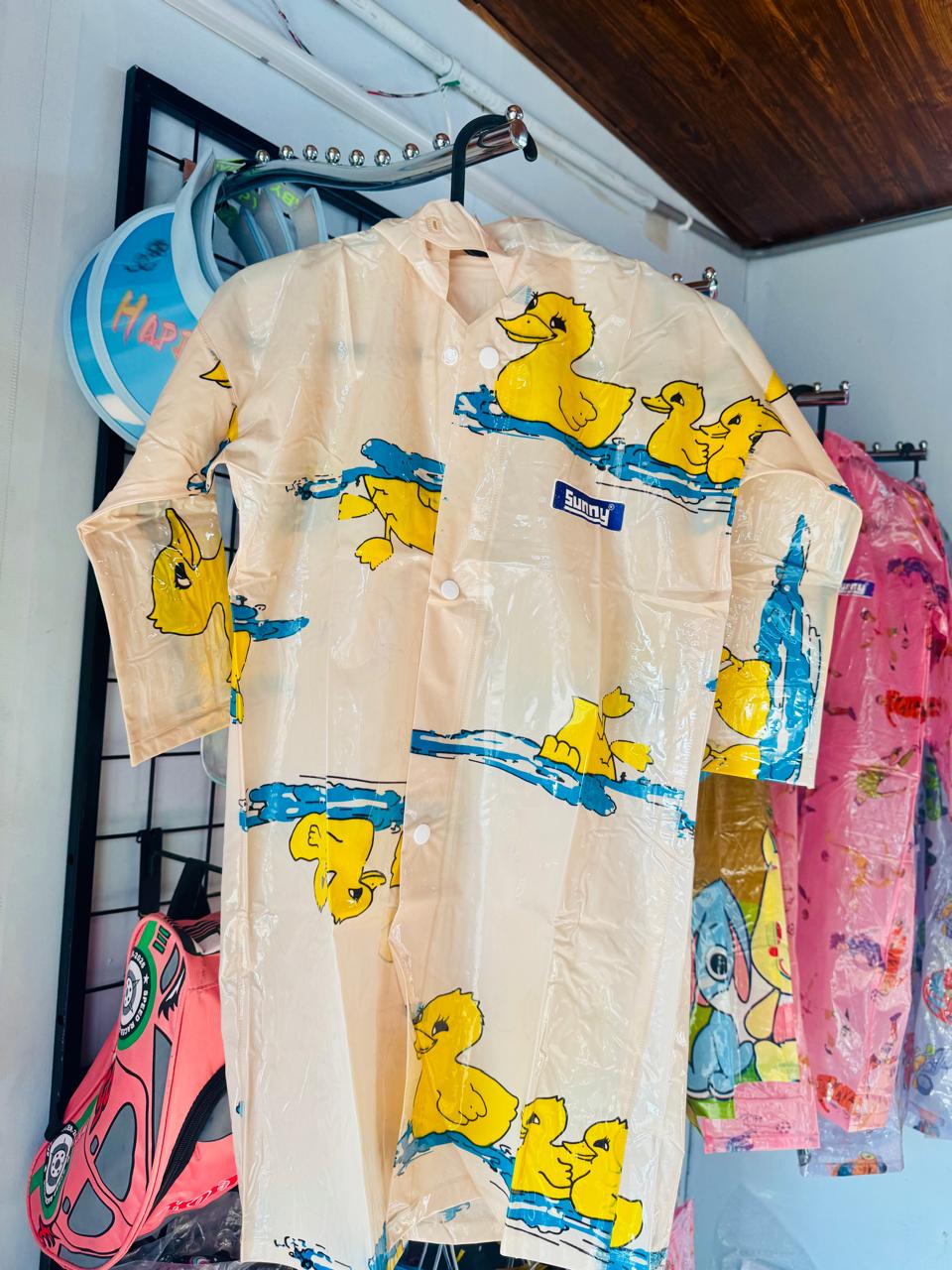 Cream duck print kids raincoat hanging on a shop display rail