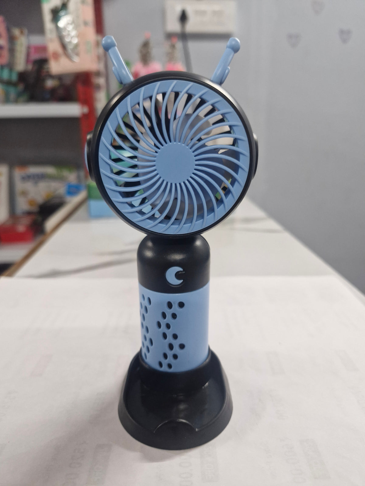 Blue and black antenna mini fan standing on a wooden table